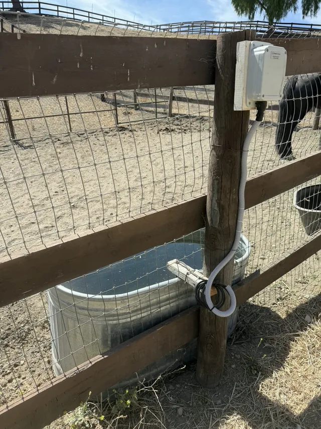 A Meterra trough monitor on a customer's galvanized water trough in Los Olivos, California, communication box mounted up a fence post