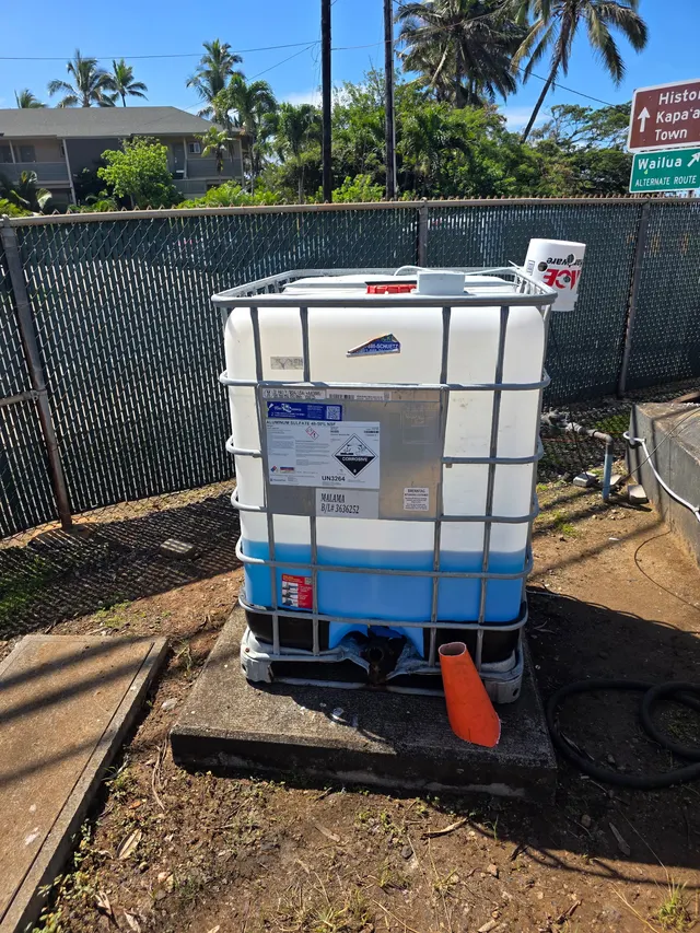 An IBC tote dosing tank in a fenced yard in Kapa'a, Hawaii, monitored by a Meterra ultrasonic tank level sensor