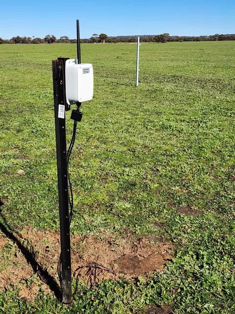 The soil probe device on a steel post in a green paddock, antenna upright, with the probes buried beside it