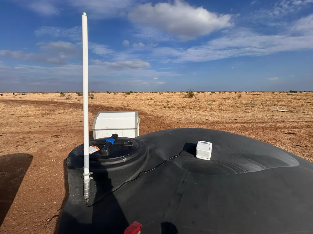 The sensor on the dome of a closed black poly tank, its cable run to a tall external antenna clamped to the fill collar