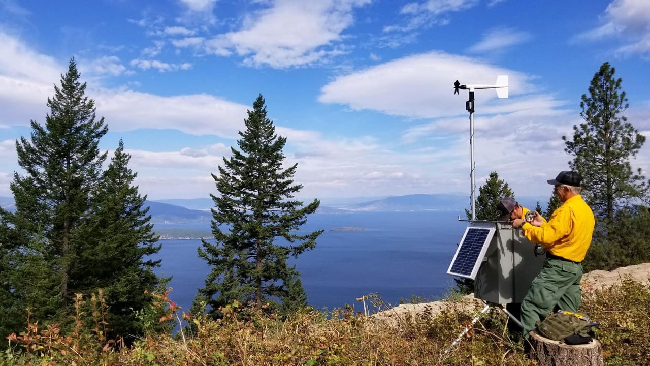 Portable solar-powered incident weather station being serviced on a ridge above a Montana lake