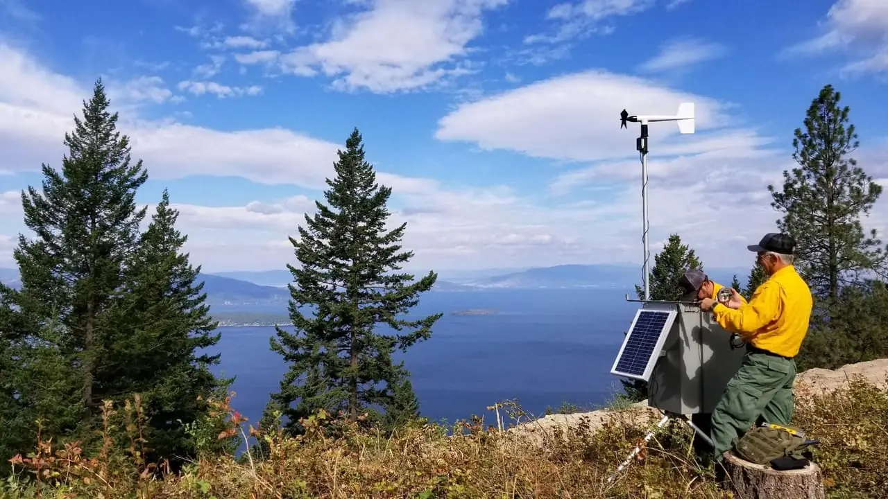 Portable solar-powered incident weather station being serviced on a ridge above a Montana lake