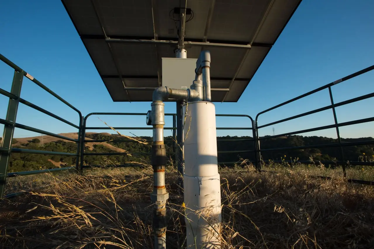 Solar-powered ranch wellhead with riser pipe and pump control box inside a stock fence