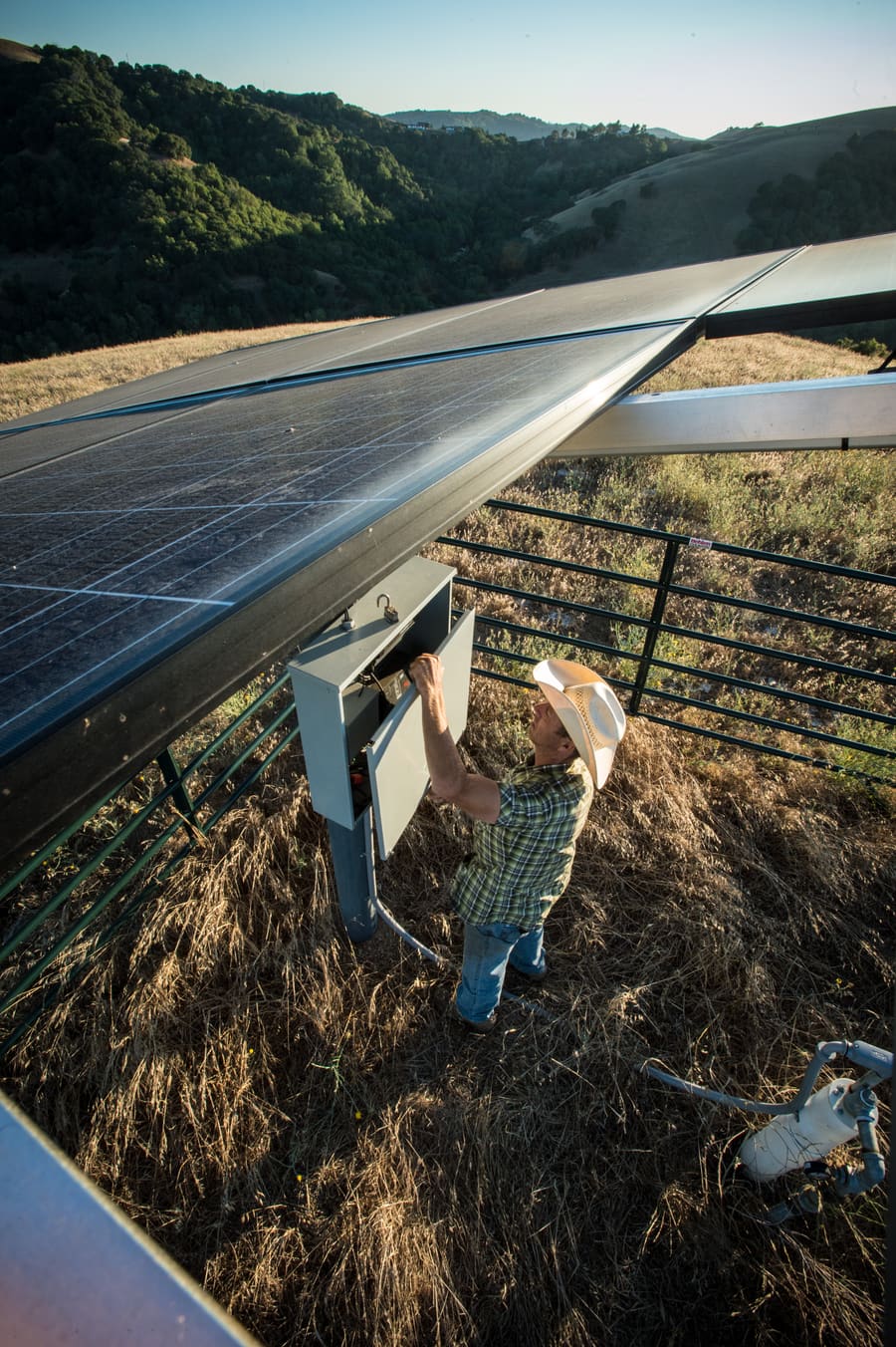 Rancher checking the pump control cabinet beneath the solar array that powers an off-grid well