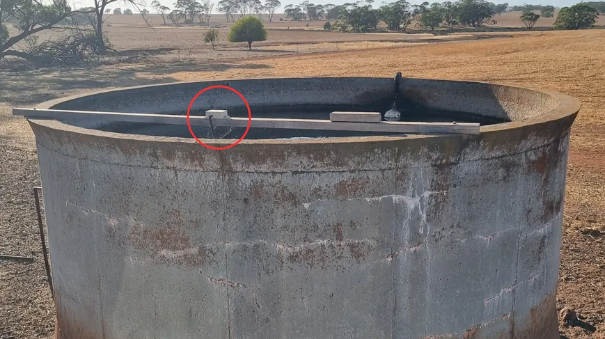 Tank level sensor on a custom bracket at the edge of an open steel tank