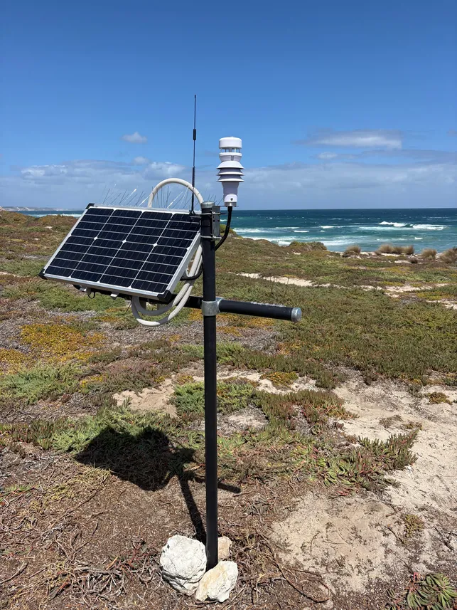 The weather station on a pole by the coast: solar panel, enclosure, and the sensor head on top