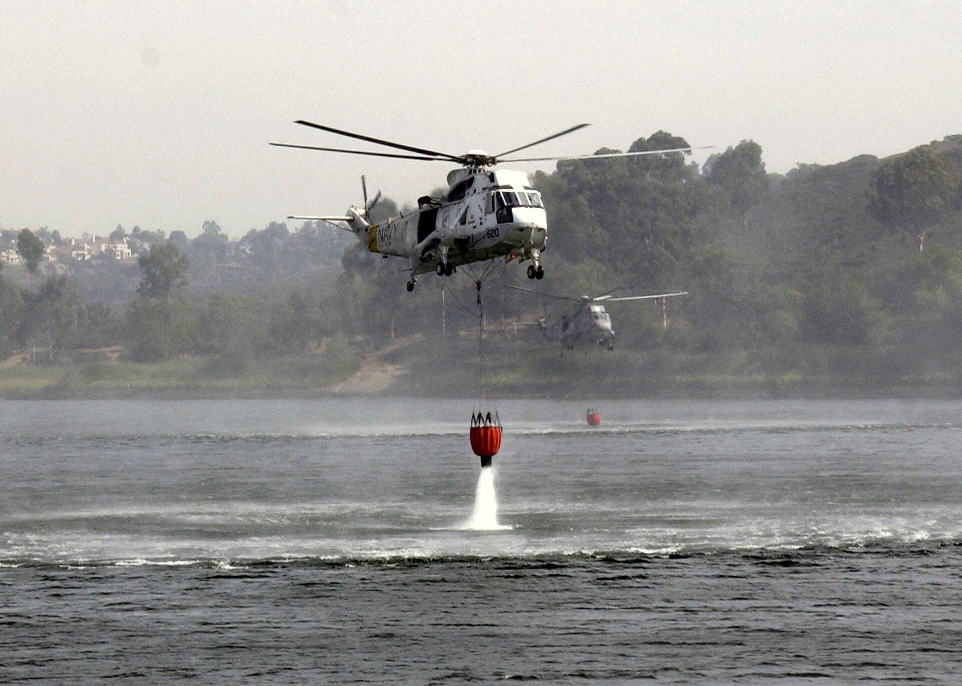 A helicopter lowers a Bambi bucket into a lake to refill during wildfire suppression operations