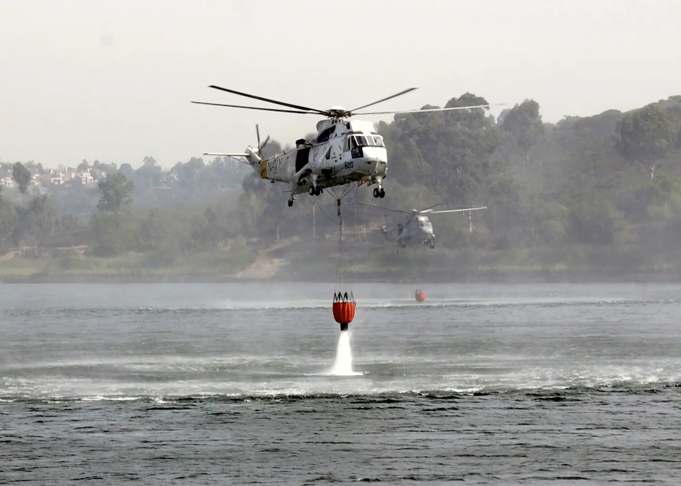 A helicopter lowers a Bambi bucket into a lake to refill during wildfire suppression operations